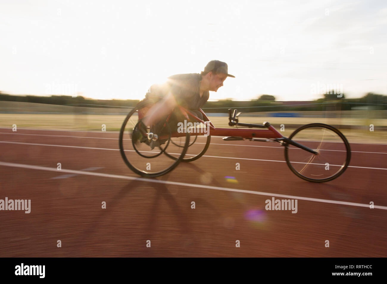Determined teenage boy paraplegic athlete speeding along sports track in wheelchair race Stock Photo