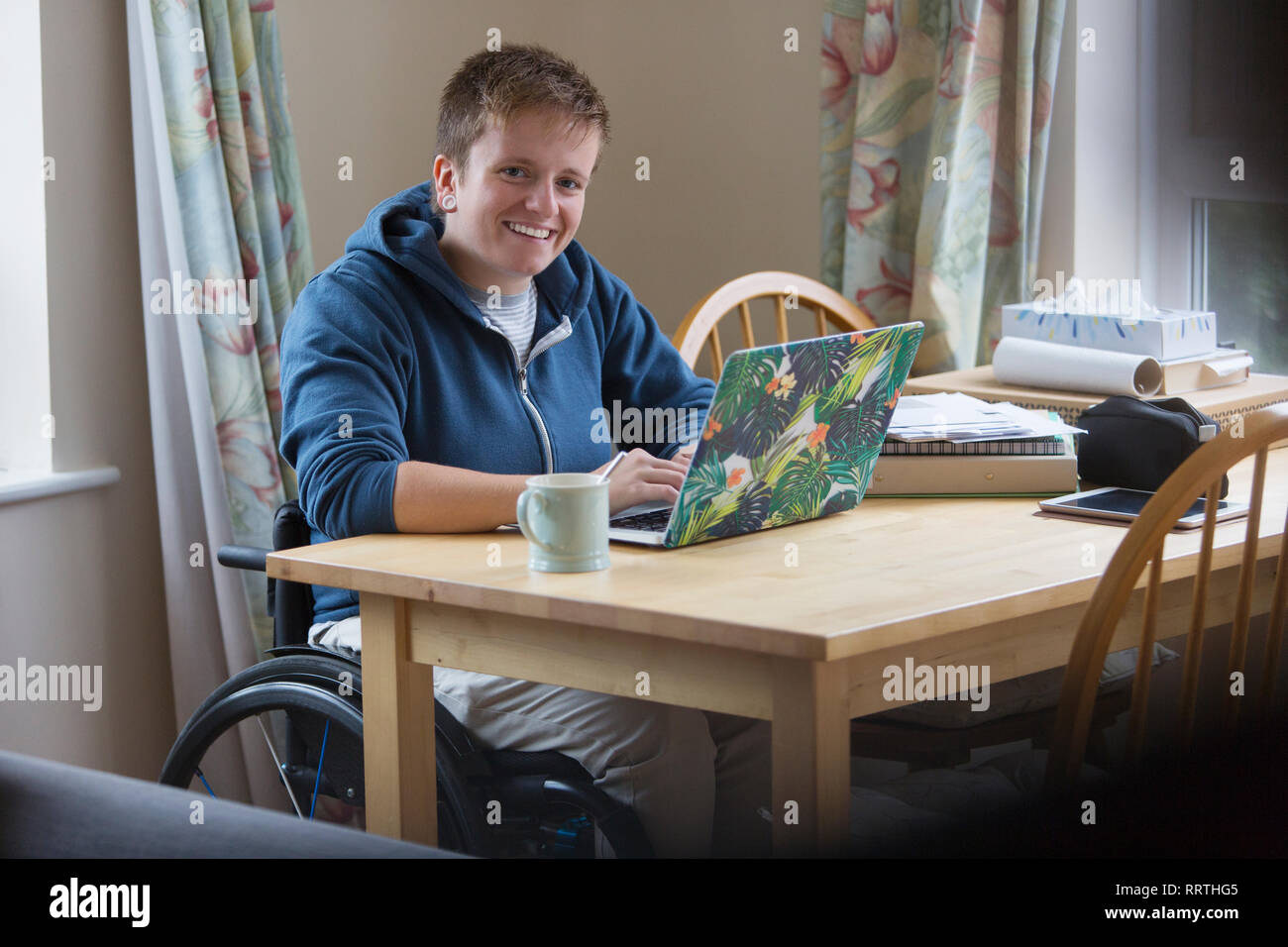 Portrait smiling, confident young woman in wheelchair using laptop at dining table Stock Photo
