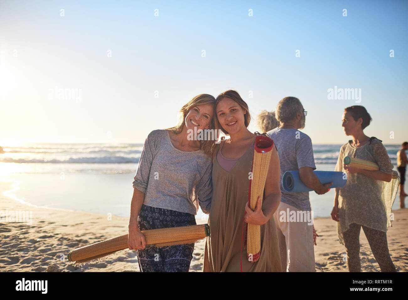 Portrait happy mother and daughter with yoga mats on sunny beach during yoga retreat Stock Photo