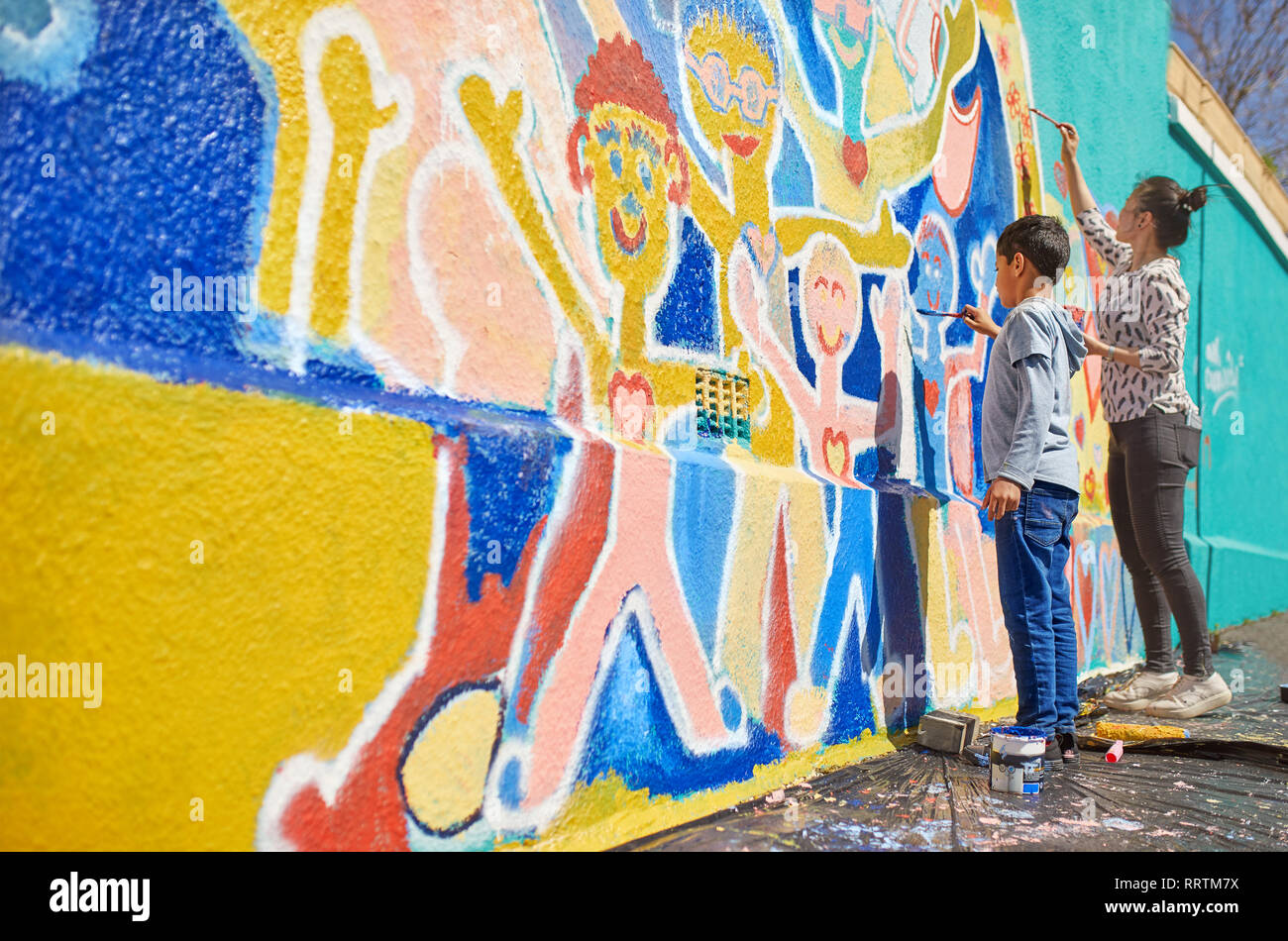 Mother and son volunteers painting vibrant mural on sunny wall Stock Photo