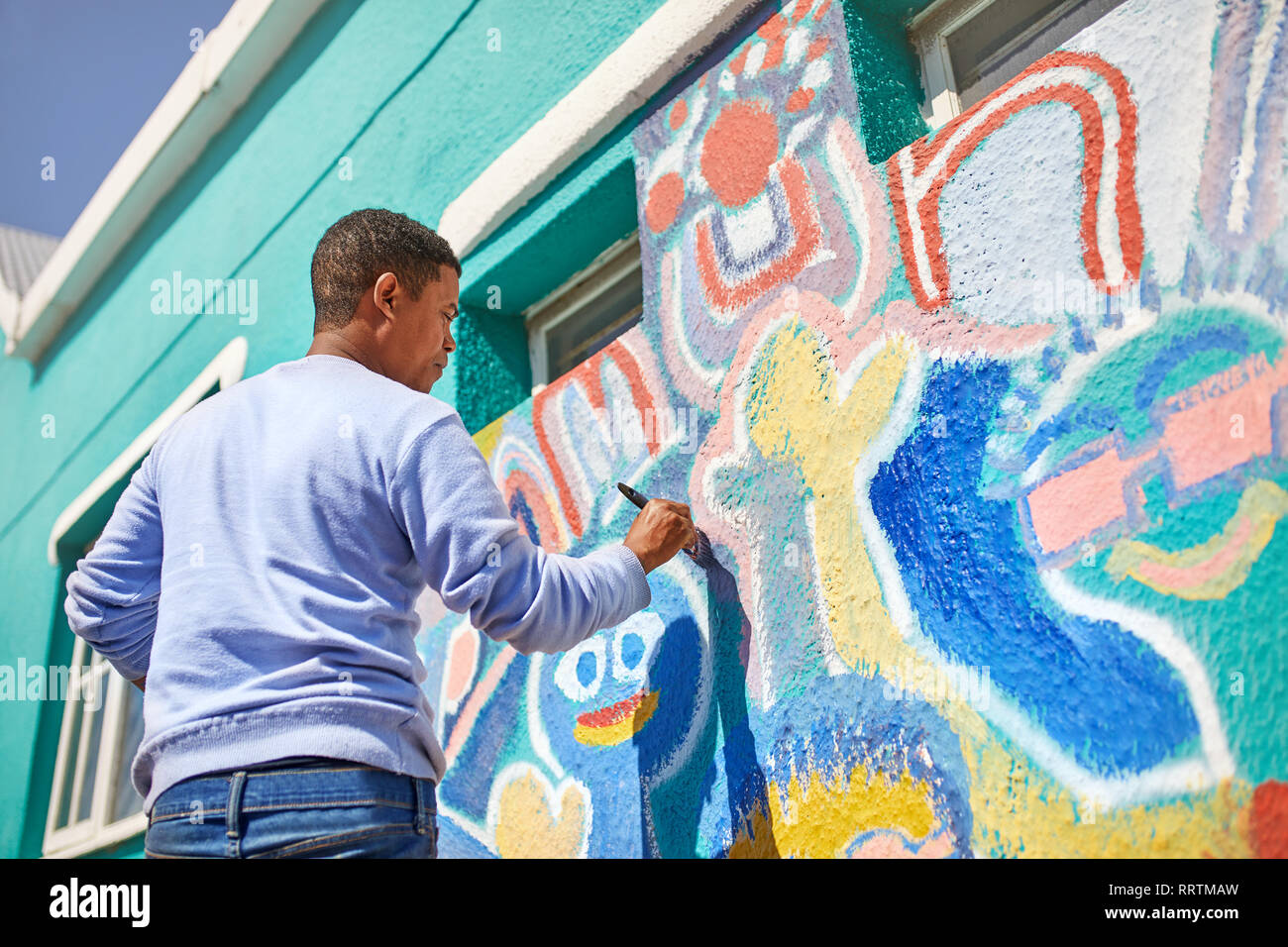 Male volunteer painting vibrant mural on sunny wall Stock Photo