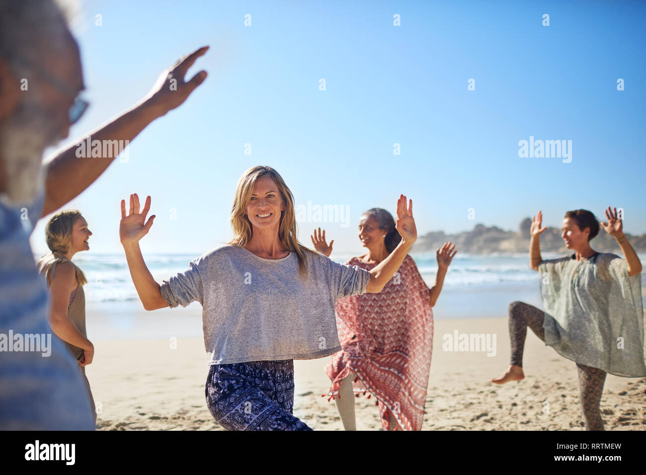 Group dancing on sunny beach during yoga retreat Stock Photo