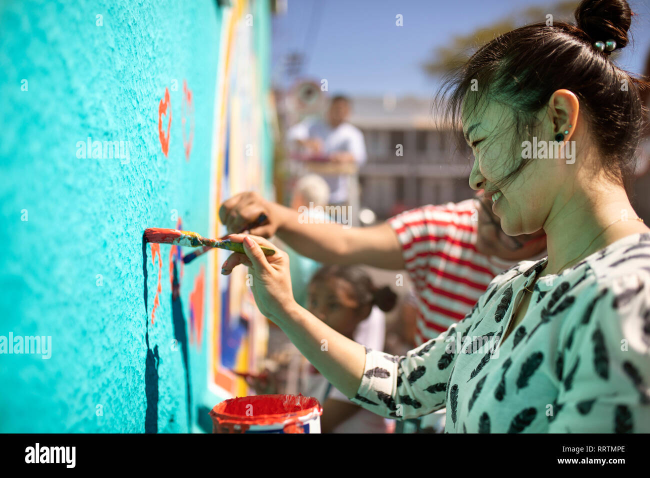 Smiling female volunteer painting mural on sunny wall Stock Photo