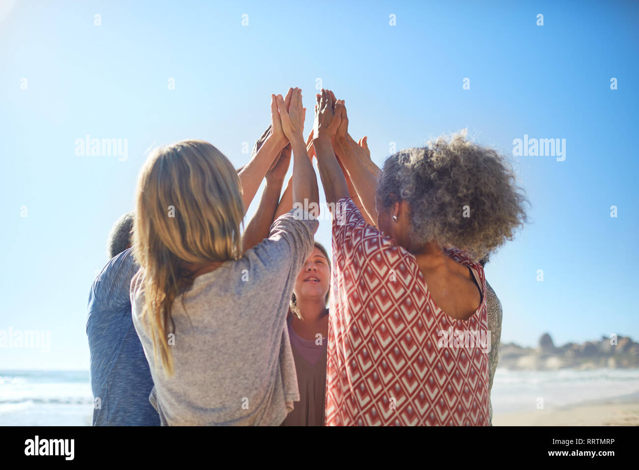 Women friends raising hands in circle during yoga retreat on sunny beach Stock Photo