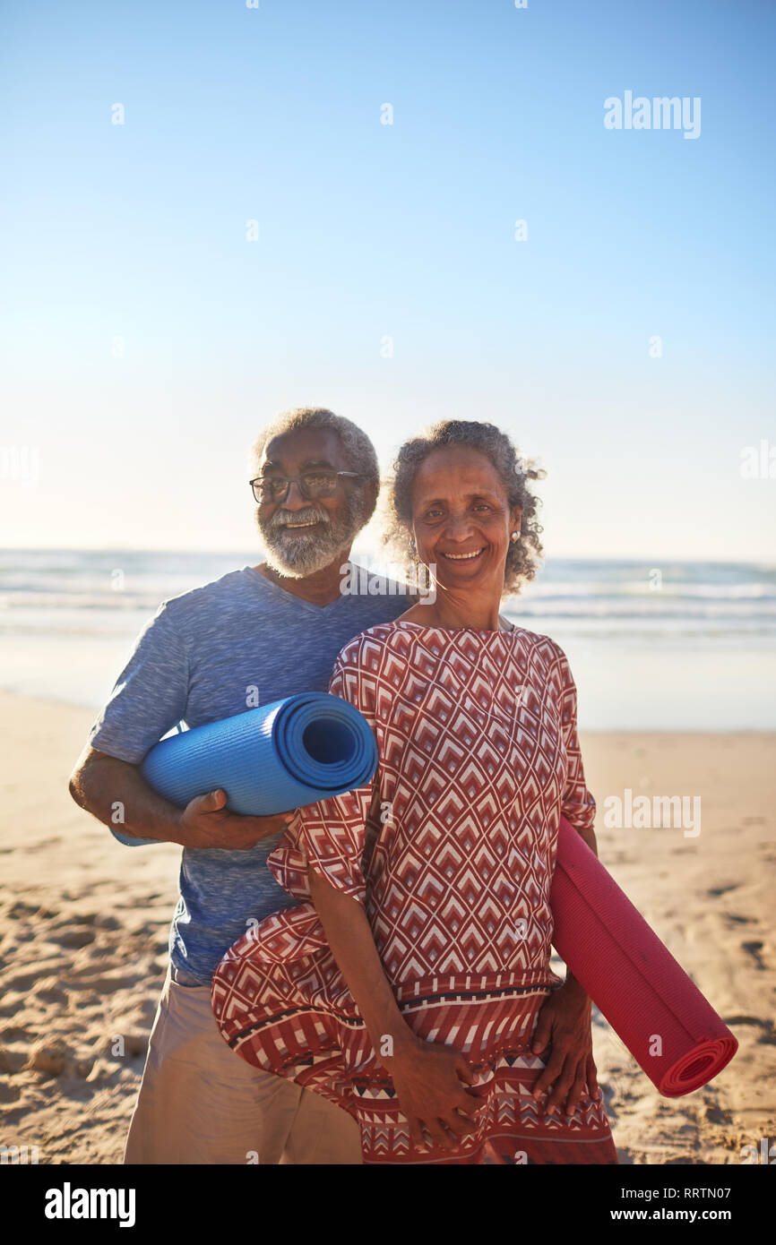 Portrait happy senior couple with yoga mats on sunny beach Stock Photo