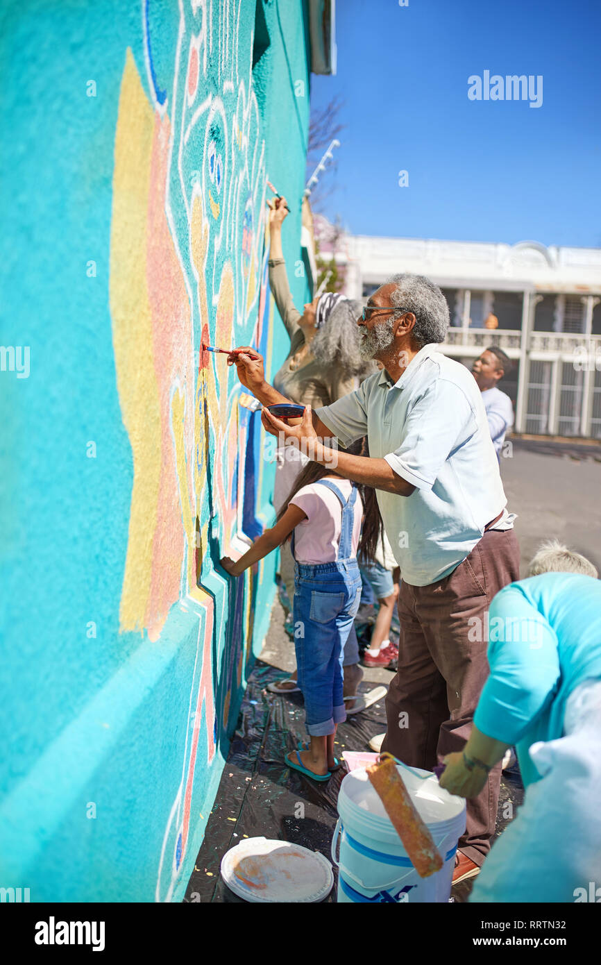Community volunteers painting vibrant mural on sunny urban wall Stock Photo