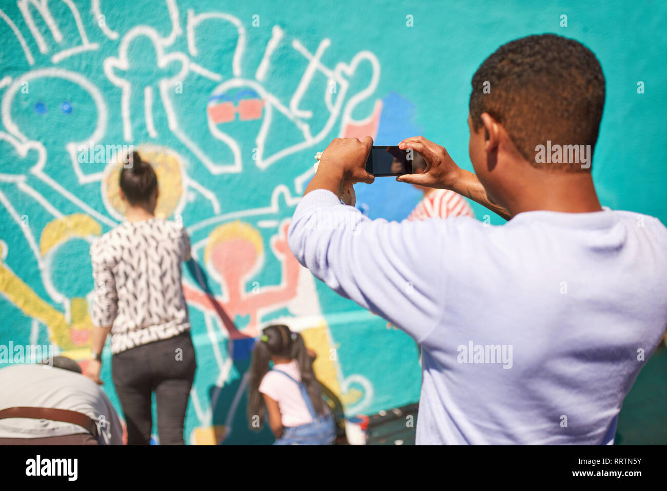 Man with camera phone photographing community mural on sunny wall Stock Photo