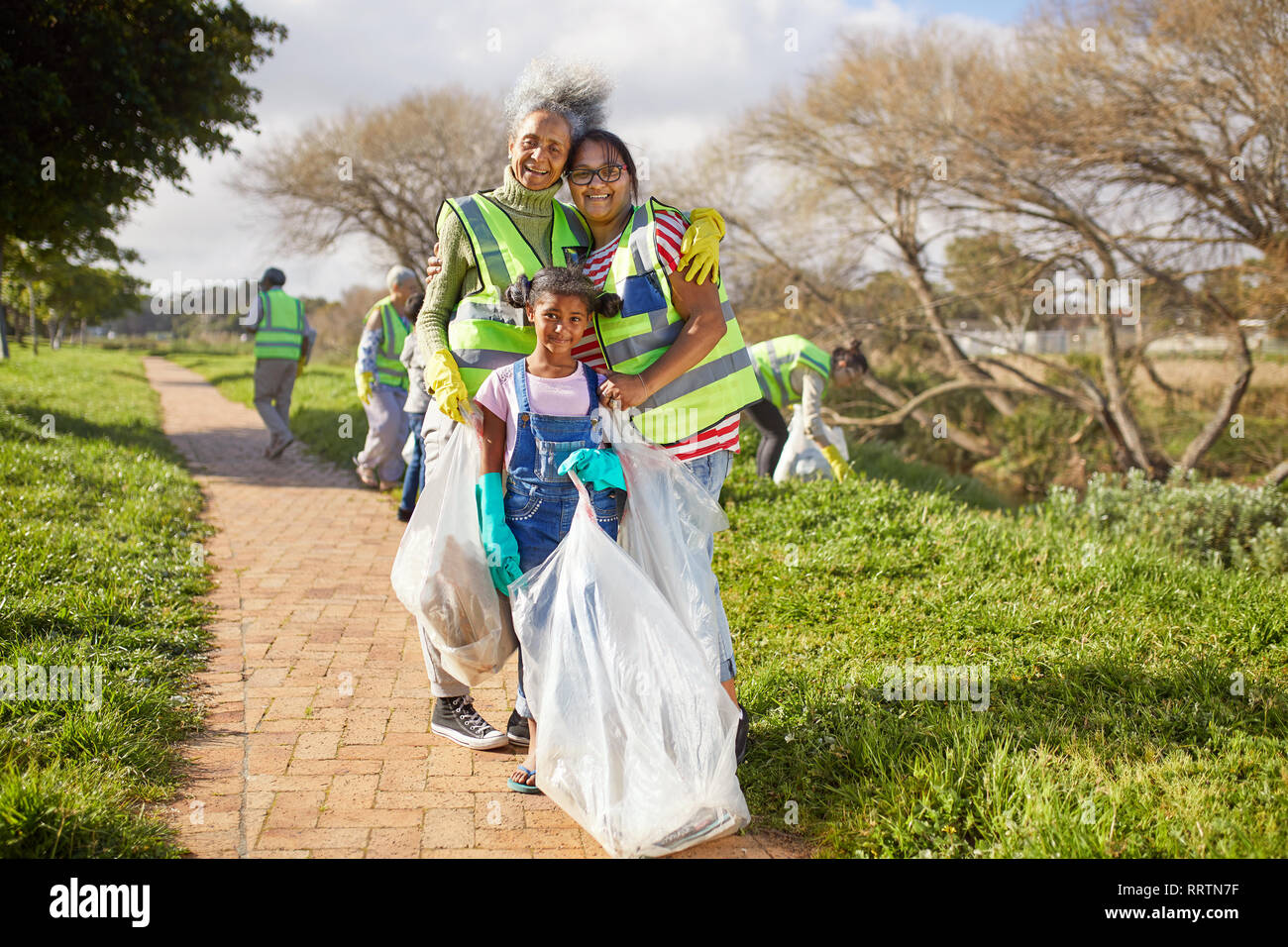 Portrait happy multi-generation women volunteering, cleaning up litter in sunny park Stock Photo