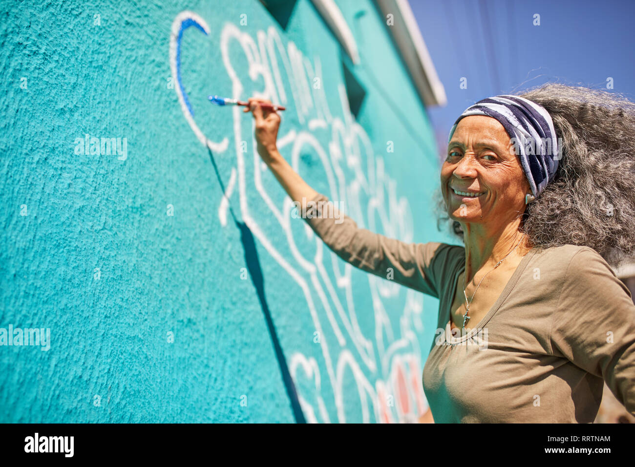 Portrait happy senior female volunteer painting on sunny wall Stock Photo