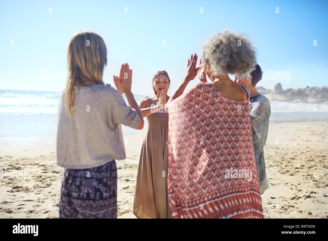 Women friends with hands clasped in circle on sunny beach during yoga retreat Stock Photo