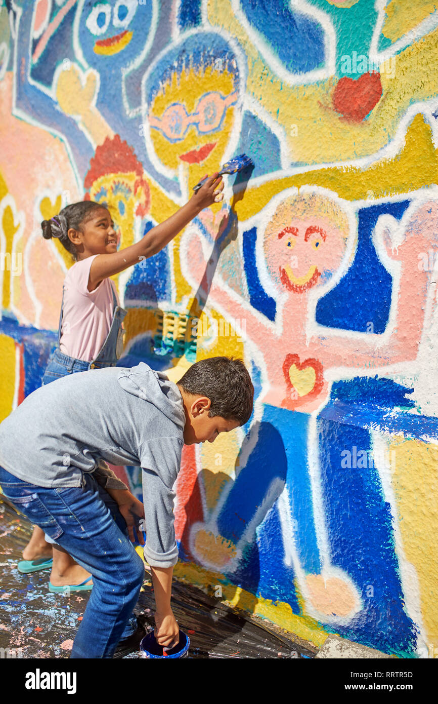 Children painting vibrant mural on sunny wall Stock Photo