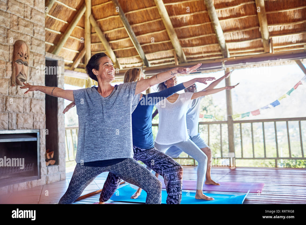 Happy woman practicing yoga warrior 2 pose in hut during yoga retreat Stock Photo