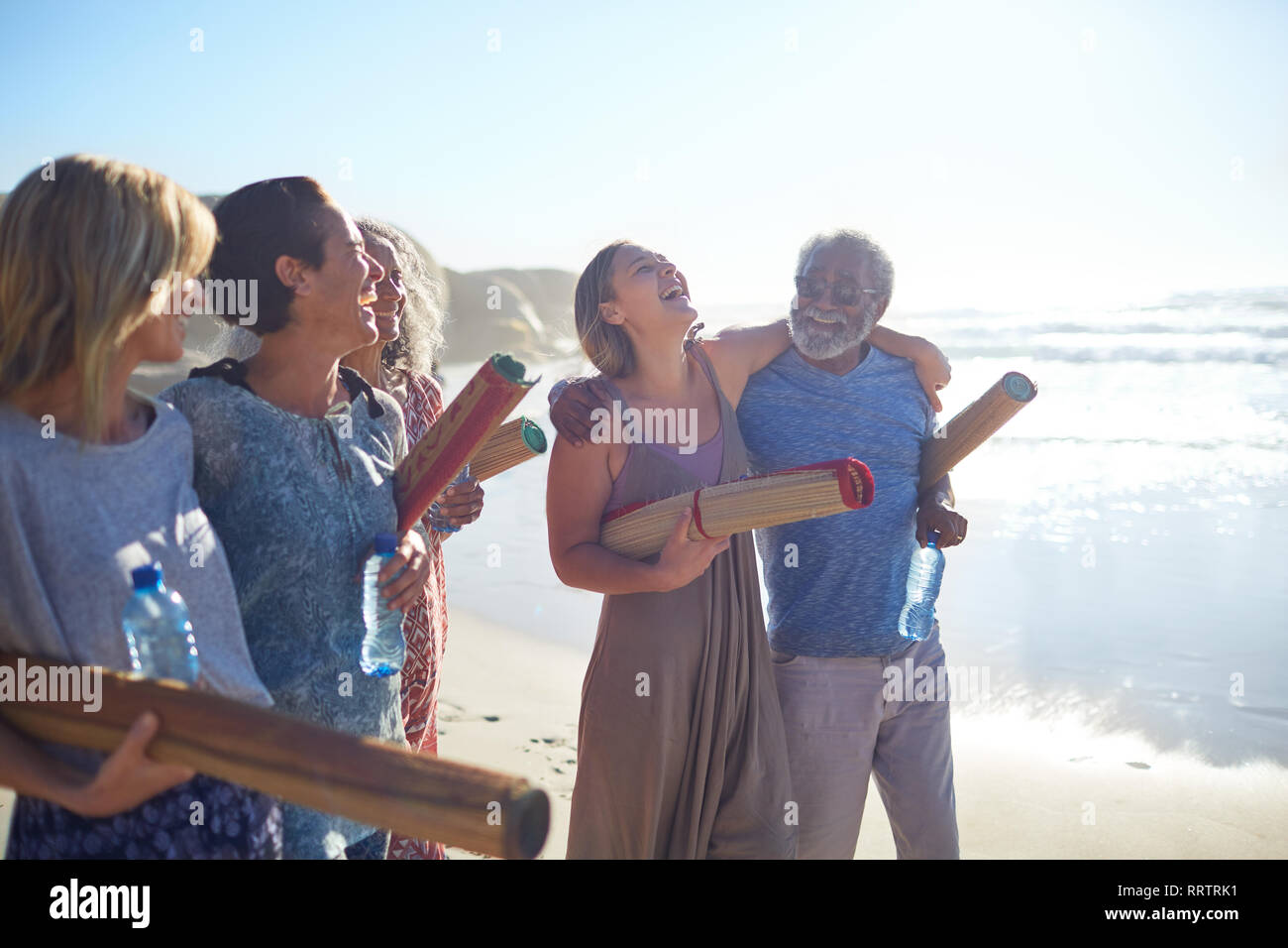 Happy friends with yoga mats bonding on sunny beach during yoga retreat Stock Photo