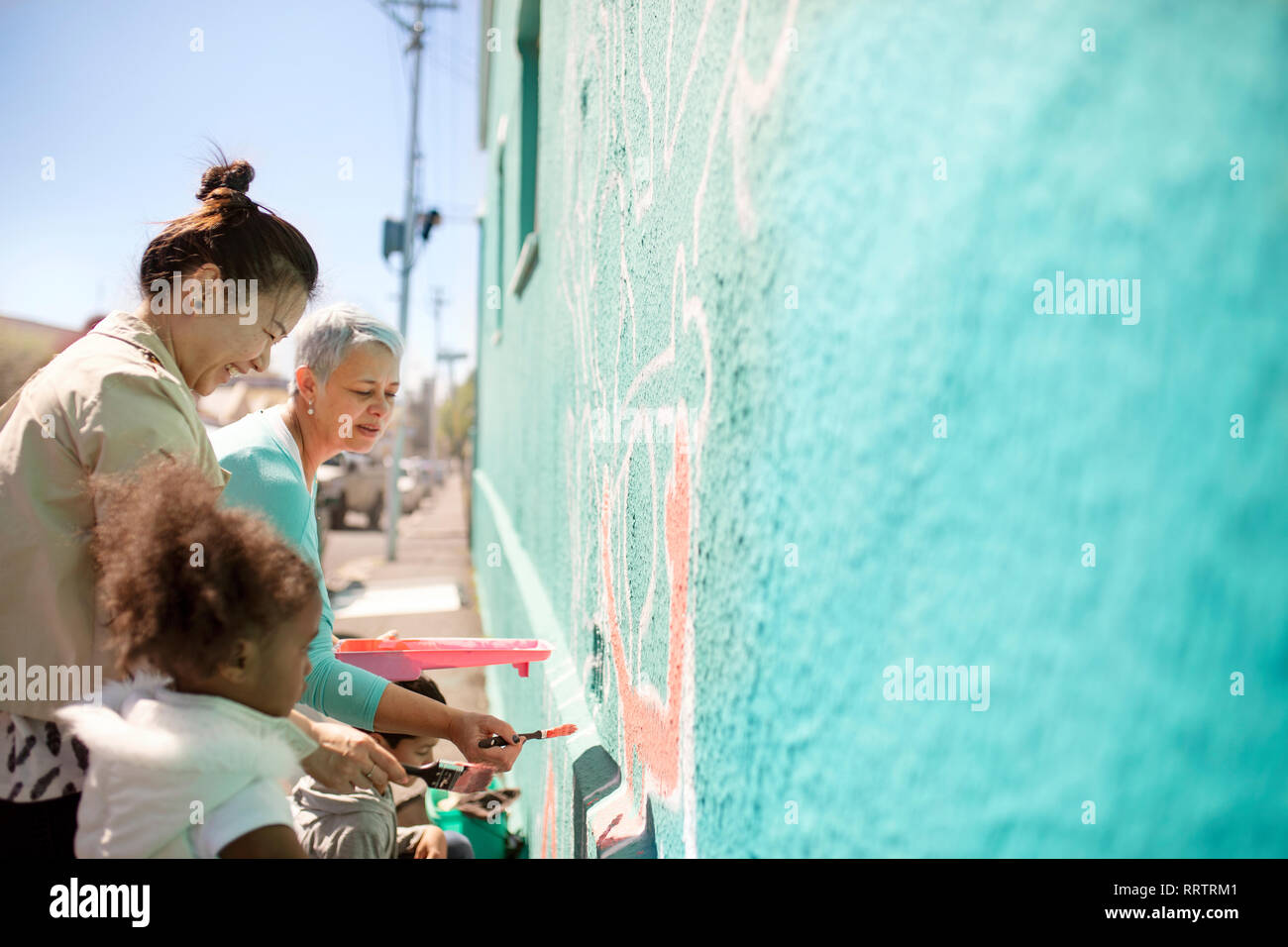 Female volunteers painting mural on sunny wall Stock Photo
