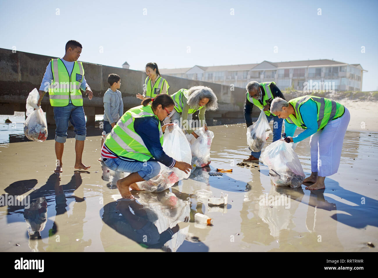Volunteers cleaning up litter on sunny, wet sand beach Stock Photo - Alamy