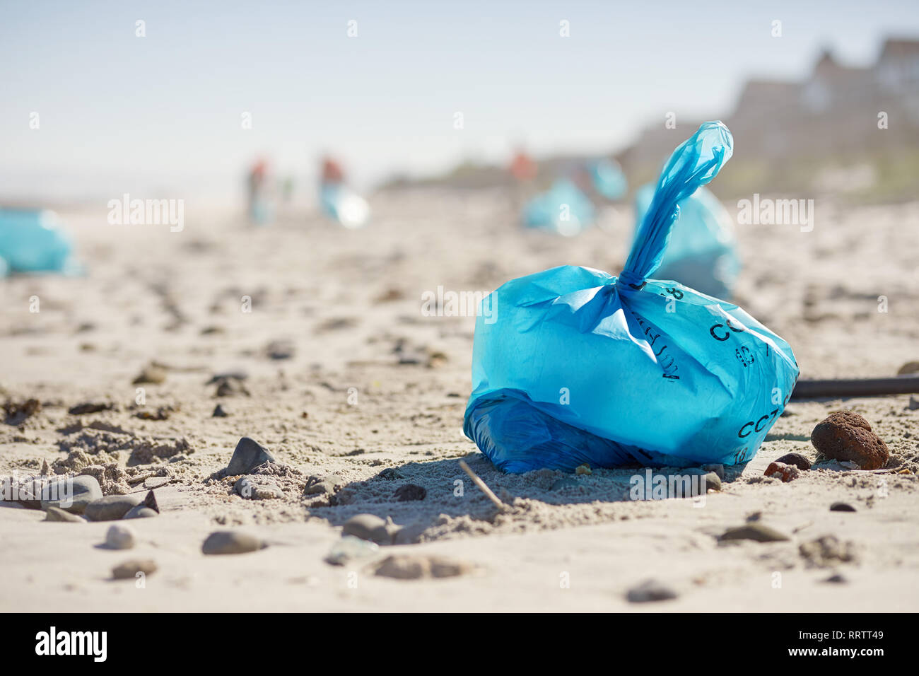 Blue bag of litter on sunny, sandy beach Stock Photo