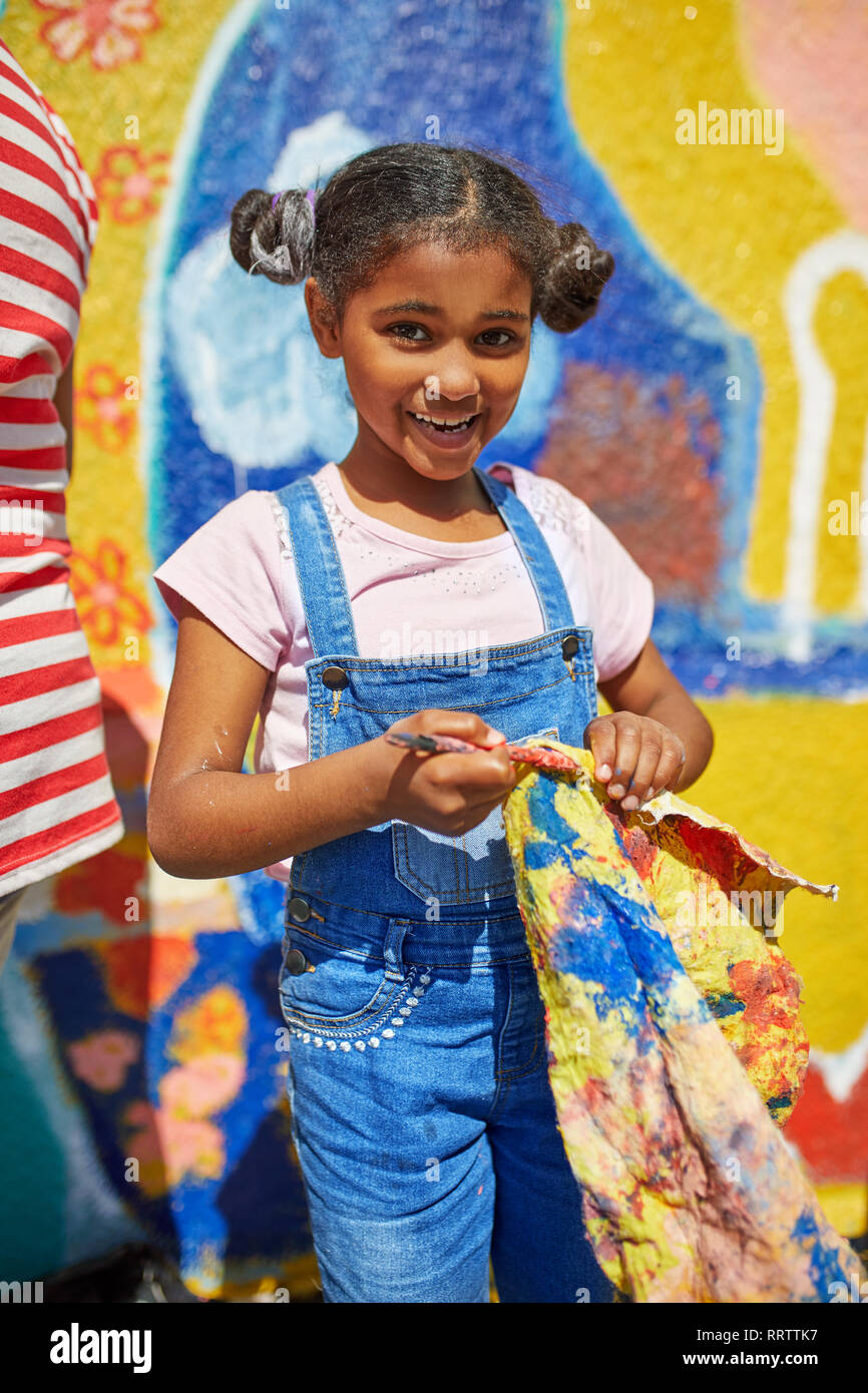 Portrait smiling girl painting vibrant mural on sunny wall Stock Photo