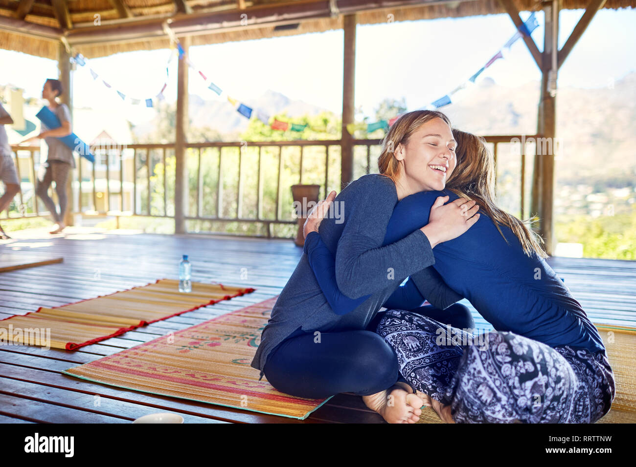 Happy mother and daughter hugging on yoga mats in hut during yoga retreat Stock Photo
