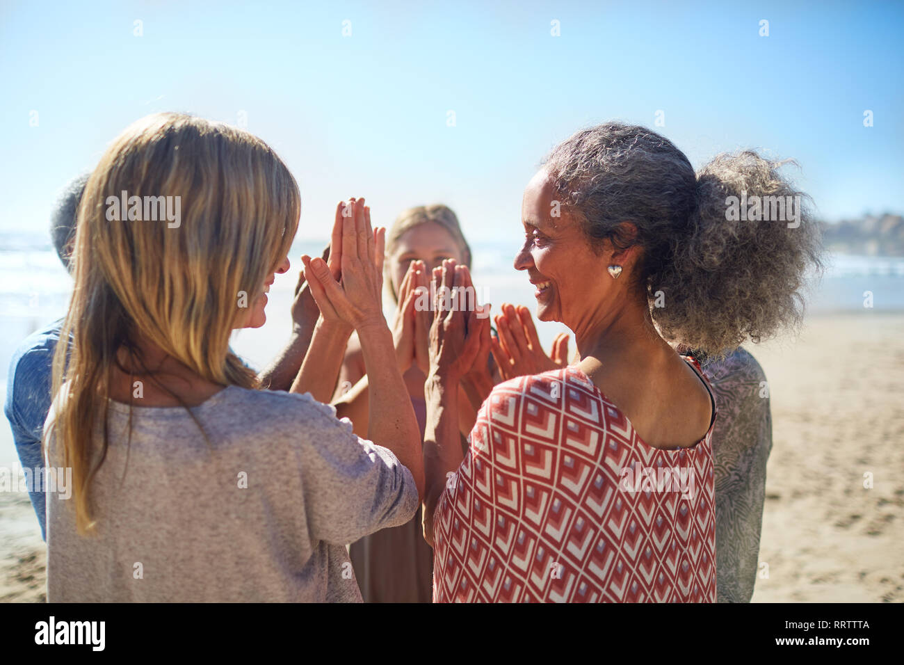 Women friends with hands clasped in circle on sunny beach during yoga retreat Stock Photo