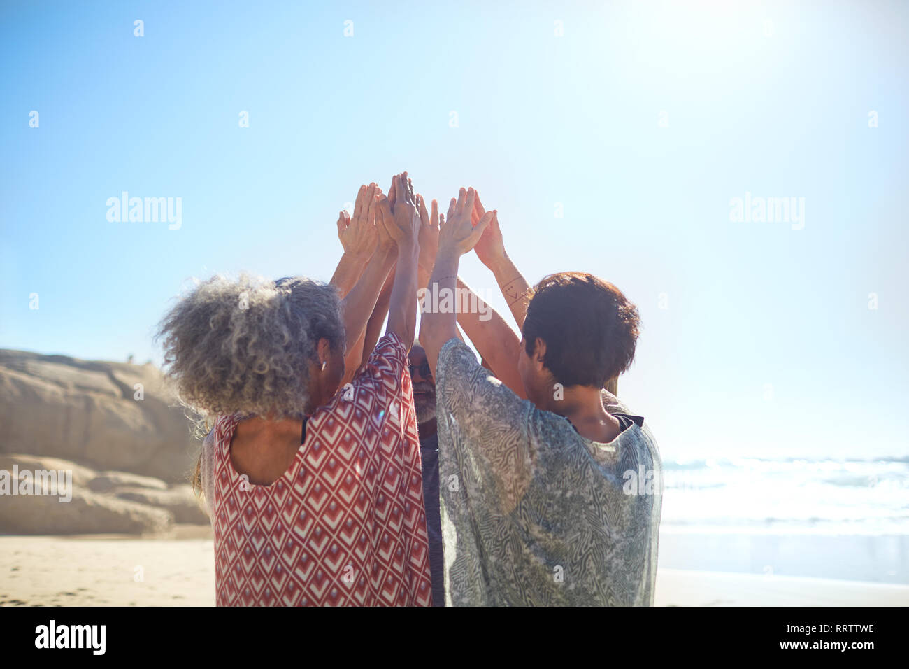 Women with arms raised in circle on sunny beach during yoga retreat Stock Photo