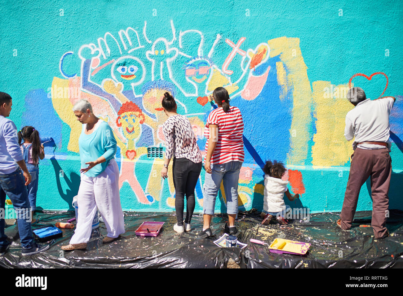 Community volunteers painting vibrant mural on sunny wall Stock Photo