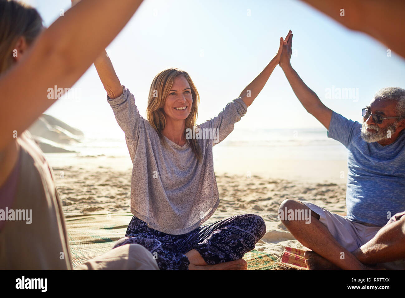 Happy friends joining hands in circle on sunny beach during yoga retreat Stock Photo