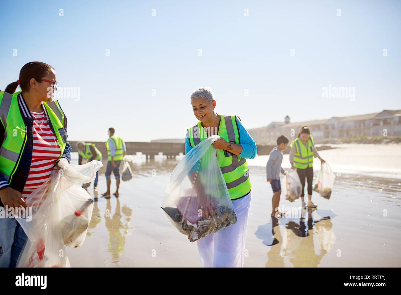Volunteers cleaning up litter on sunny, wet sand beach Stock Photo