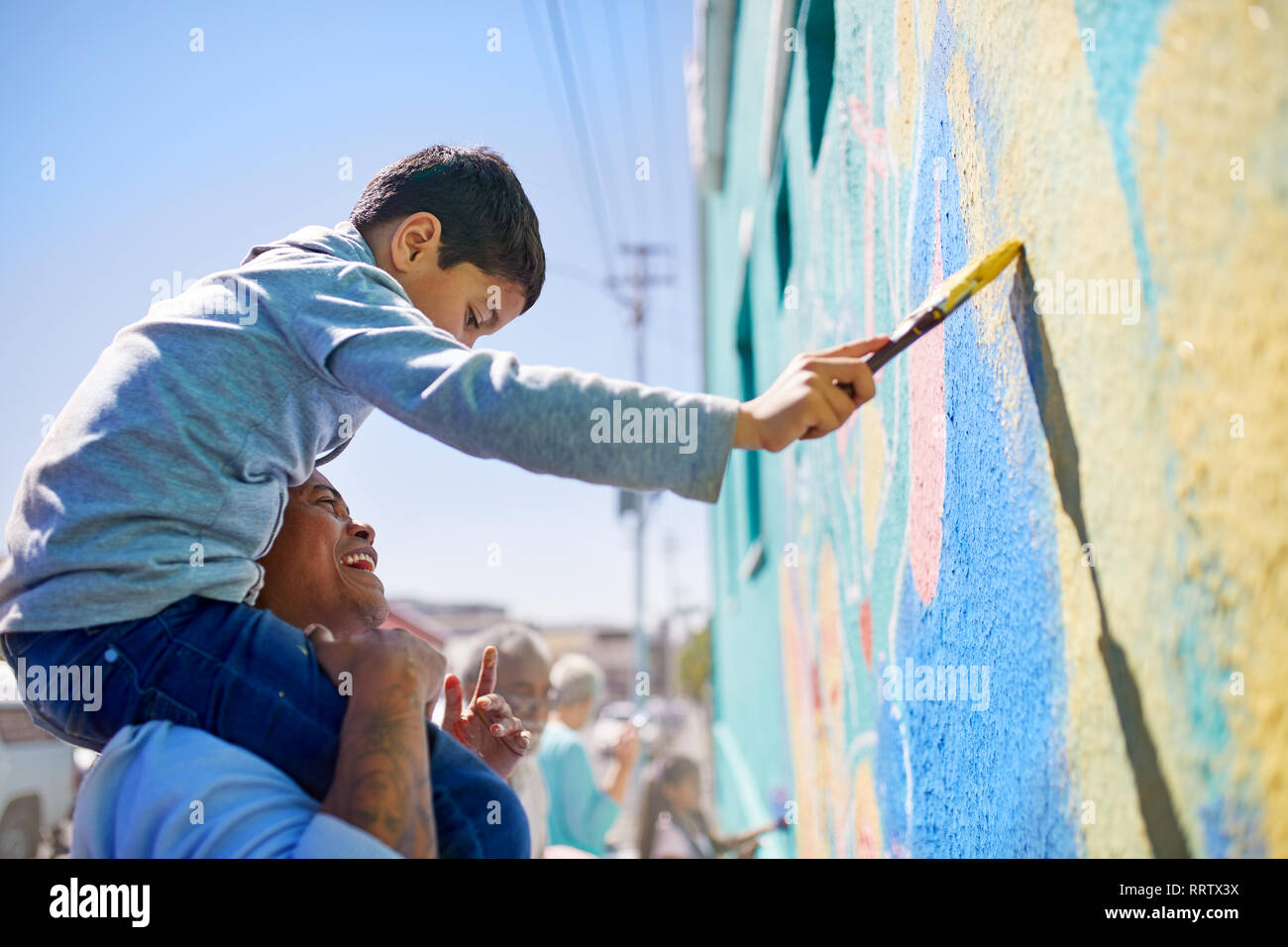 Father and son volunteers painting mural on sunny wall Stock Photo