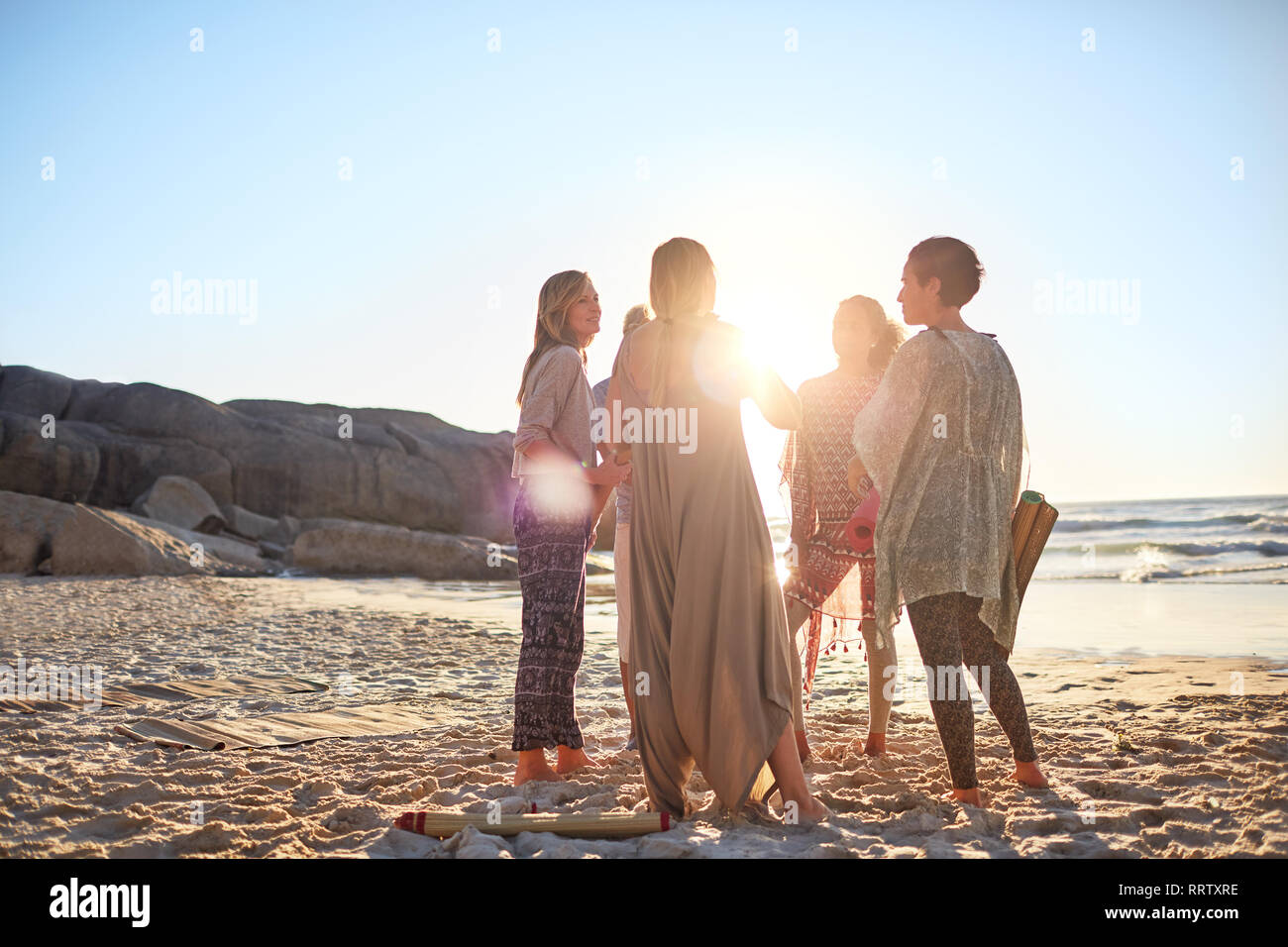 Women standing in circle on sunny beach during yoga retreat Stock Photo