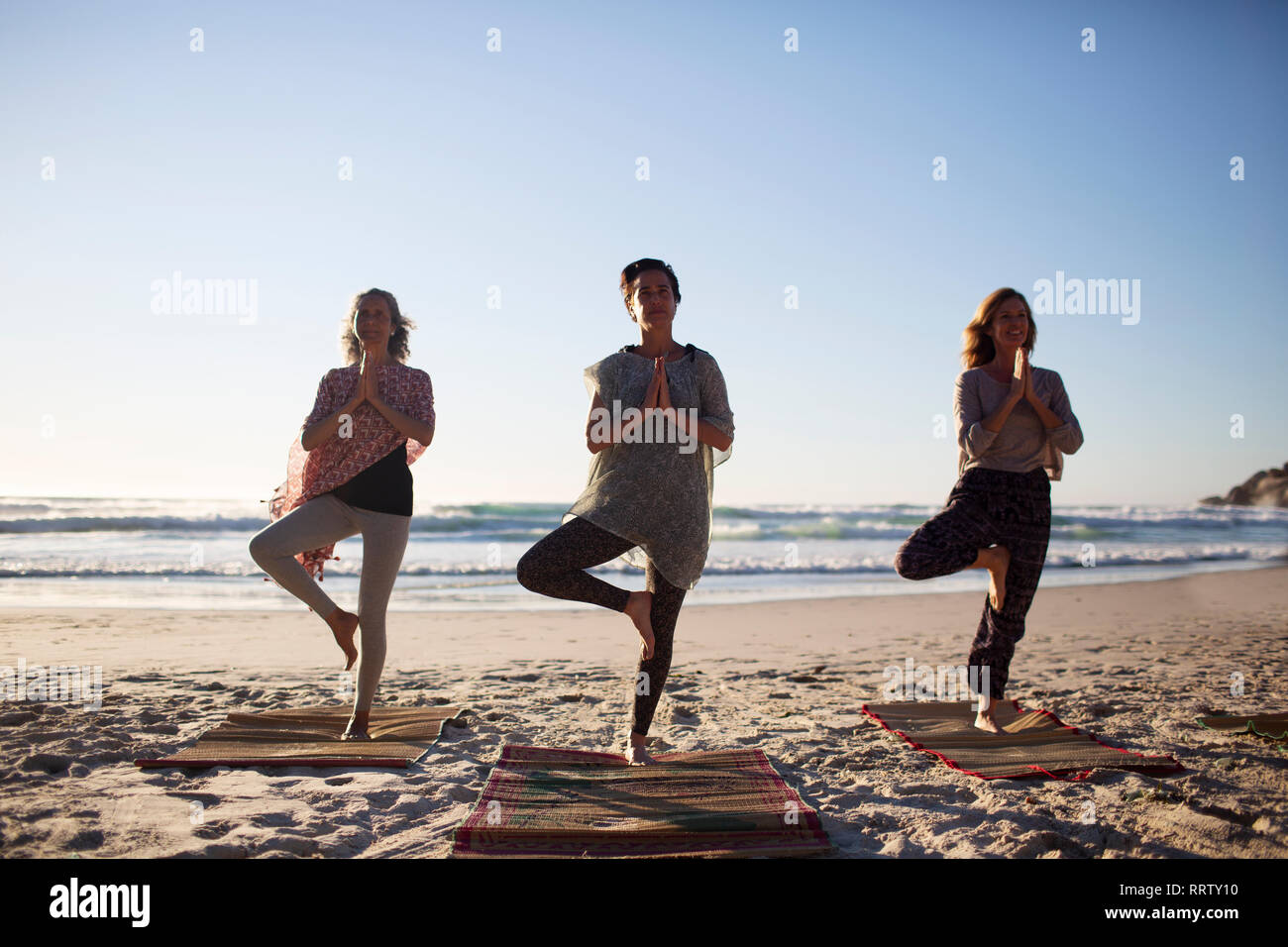 Serene women practicing yoga tree pose on sunny beach during yoga retreat Stock Photo