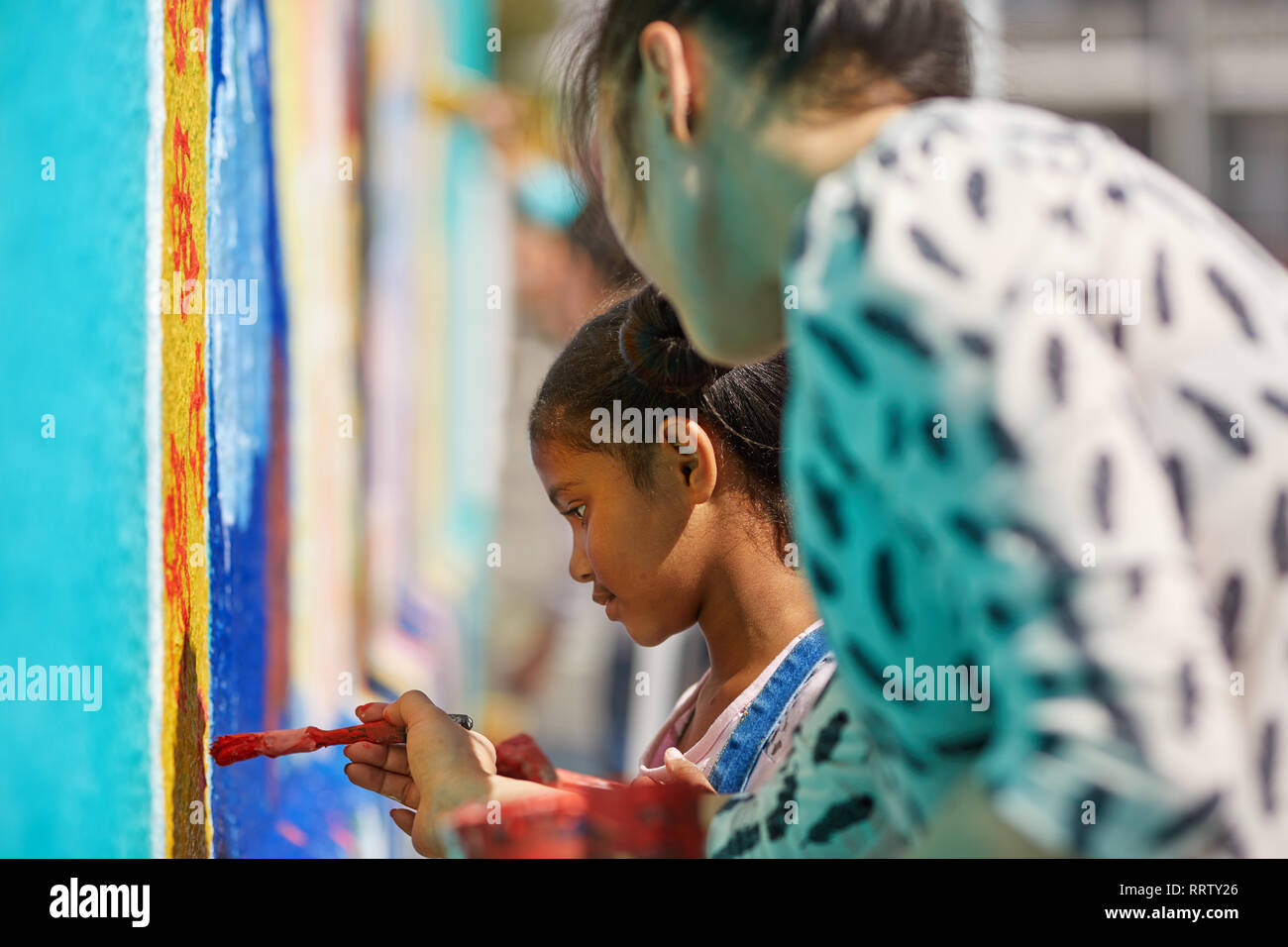 Teacher and elementary girl student painting on wall Stock Photo