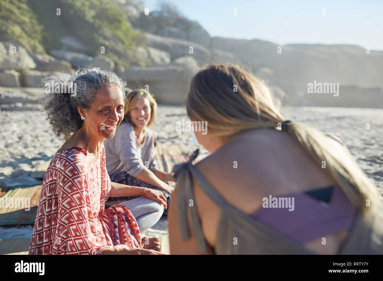 Smiling women friends talking on sunny beach during yoga retreat Stock Photo