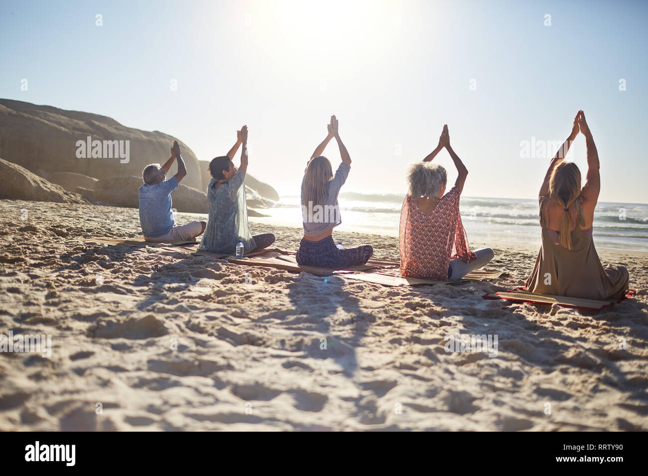 Group practicing yoga on sunny beach during yoga retreat Stock Photo