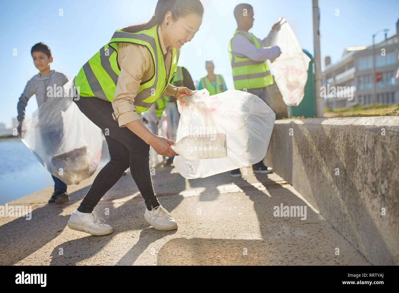 Woman volunteer picking up plastic litter on sunny boardwalk Stock Photo