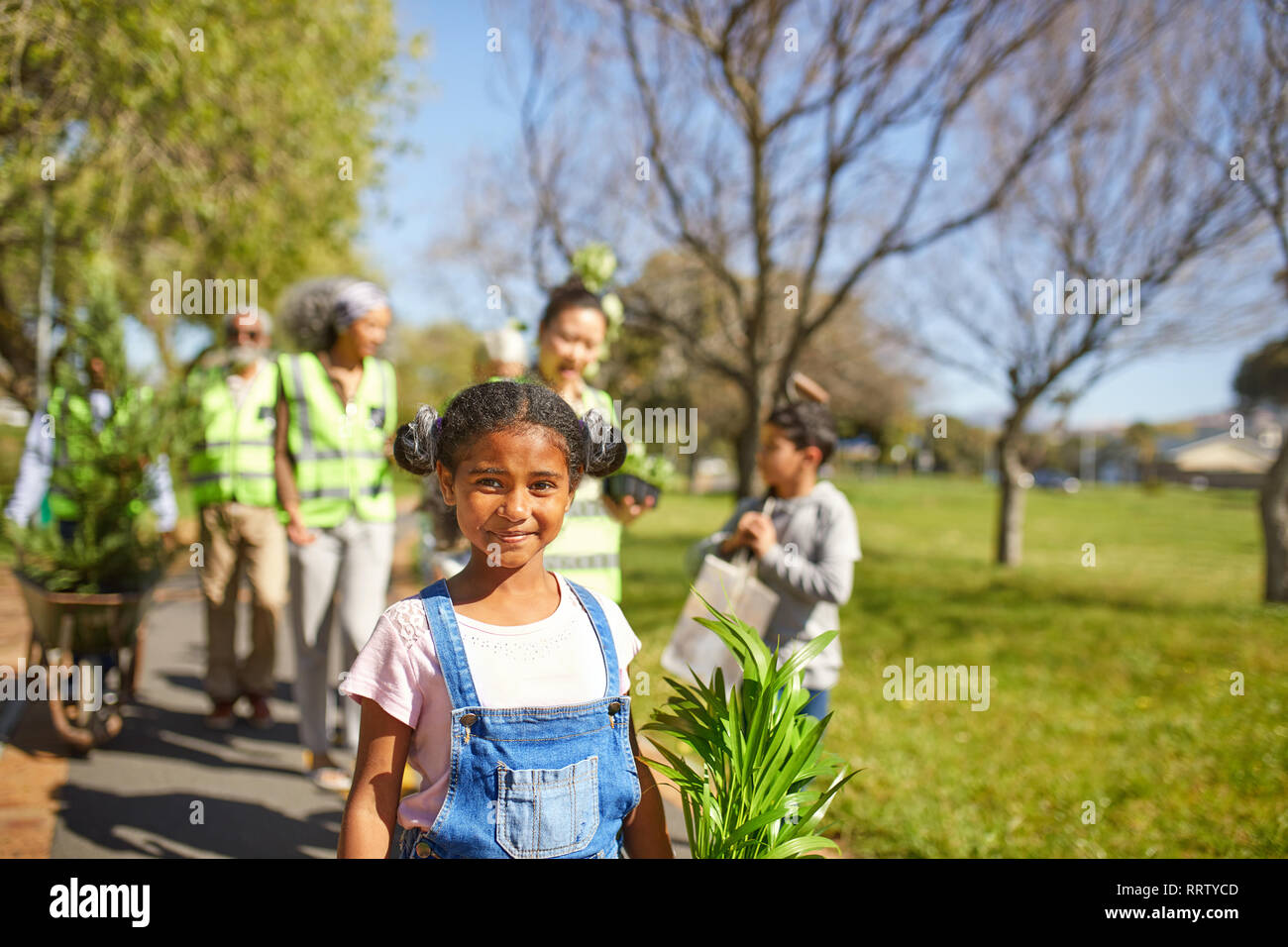 Portrait smiling, confident girl volunteering, planting trees in sunny park Stock Photo