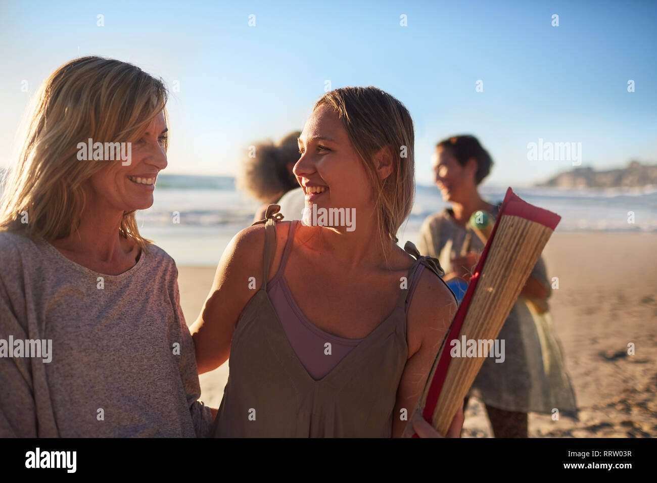 Happy mother and daughter with yoga mat on sunny beach during yoga retreat Stock Photo