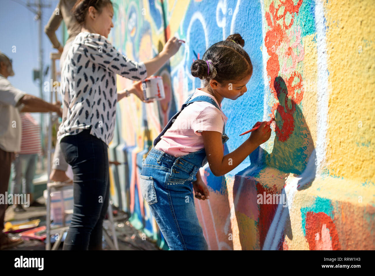Girl volunteer painting vibrant mural on sunny wall Stock Photo