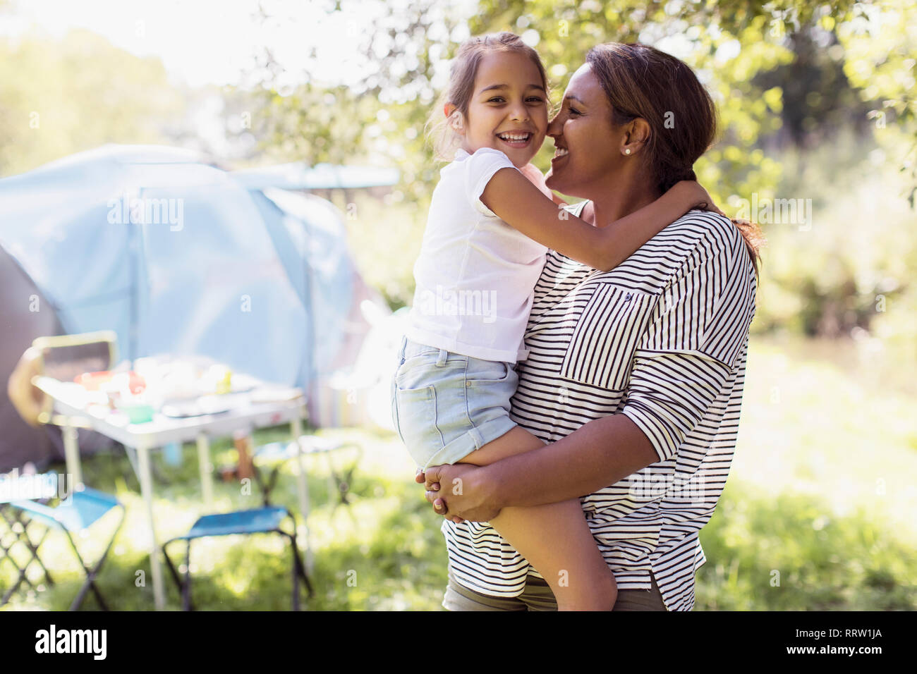 Portrait affectionate mother and daughter hugging at sunny campsite Stock Photo