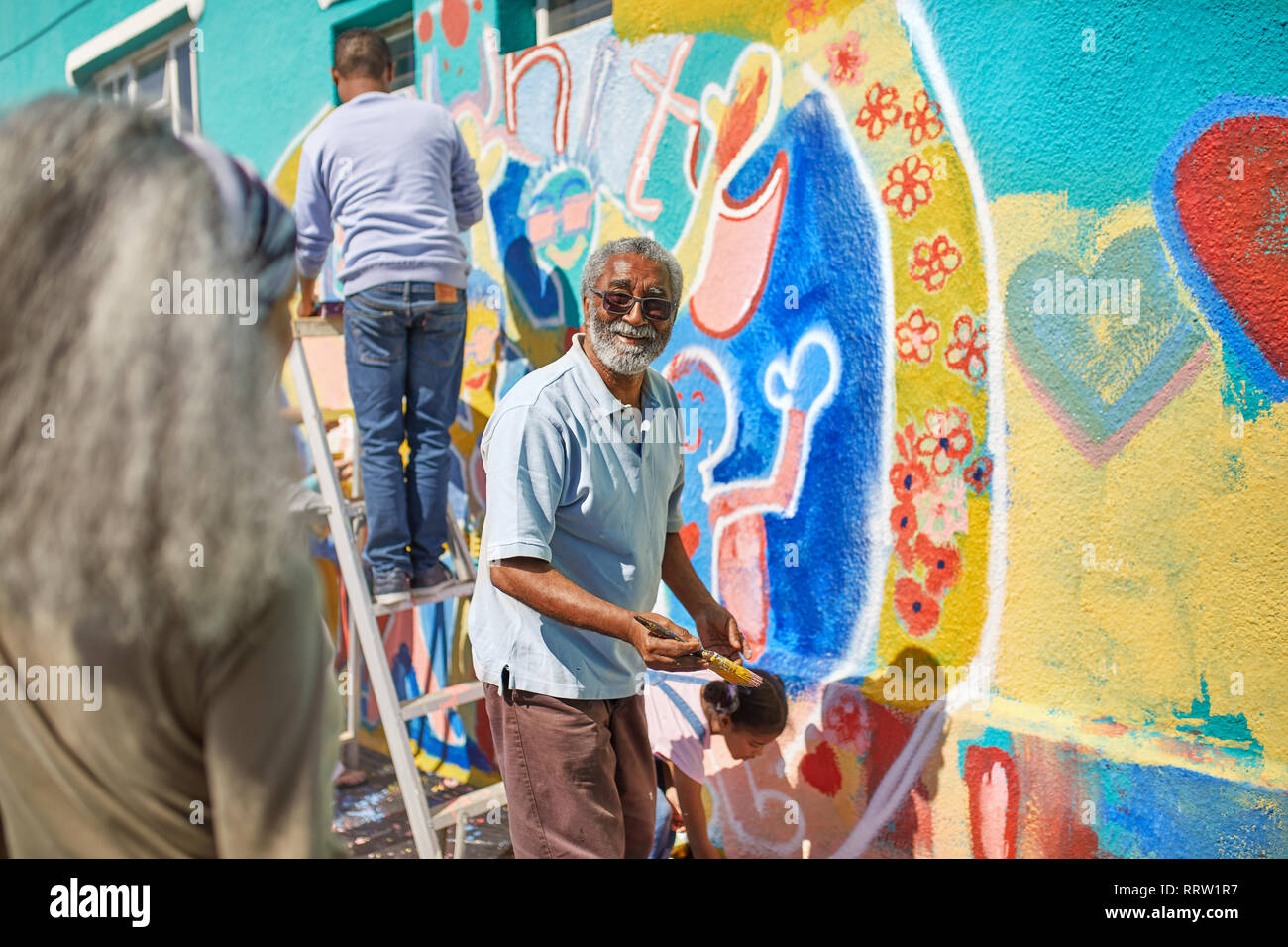 Senior man volunteer painting vibrant mural on sunny wall Stock Photo