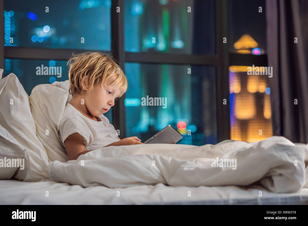 The boy uses the tablet in his bed before going to sleep on a