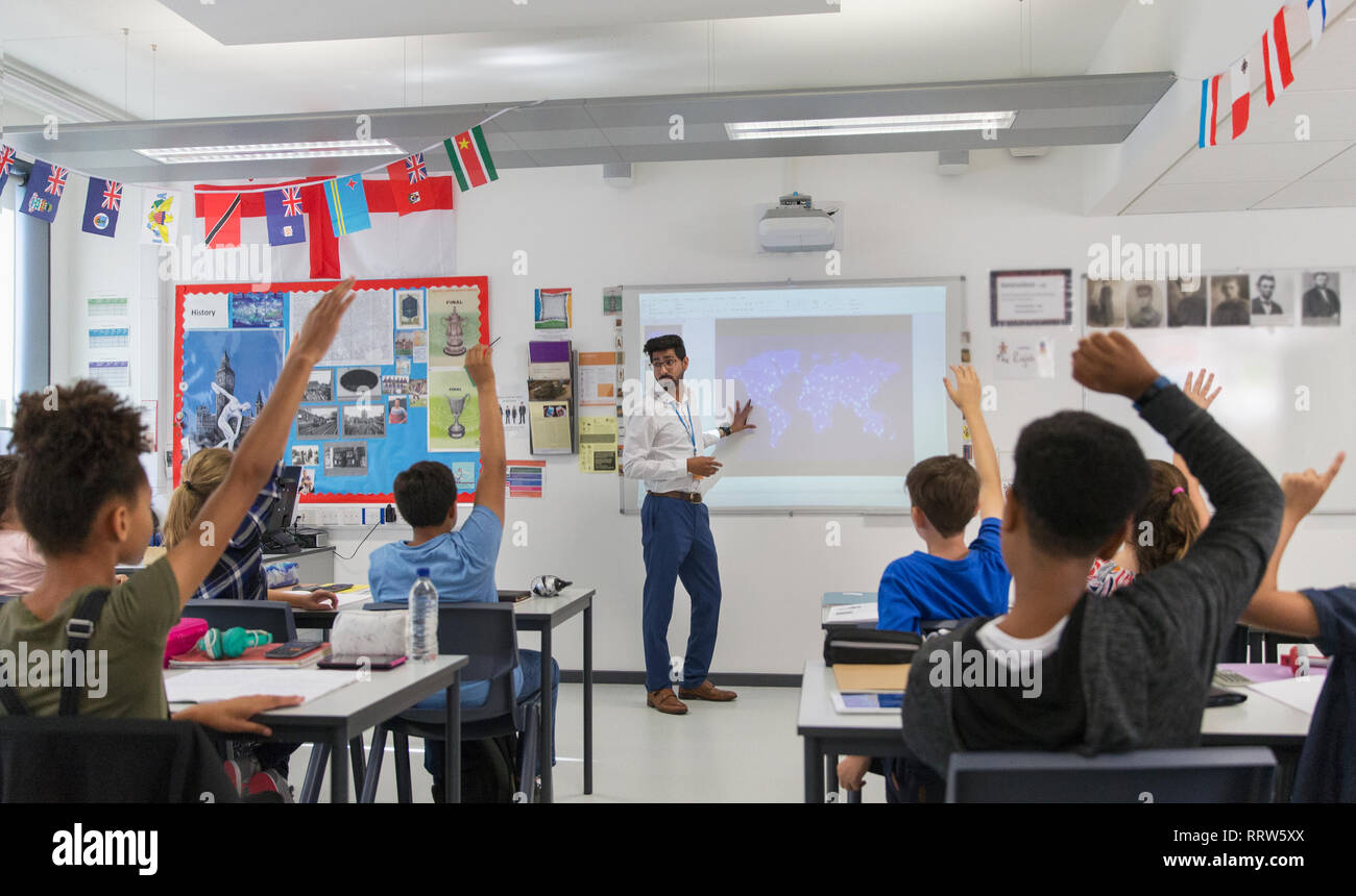 Junior high school students raising hands for teacher leading lesson in classroom Stock Photo