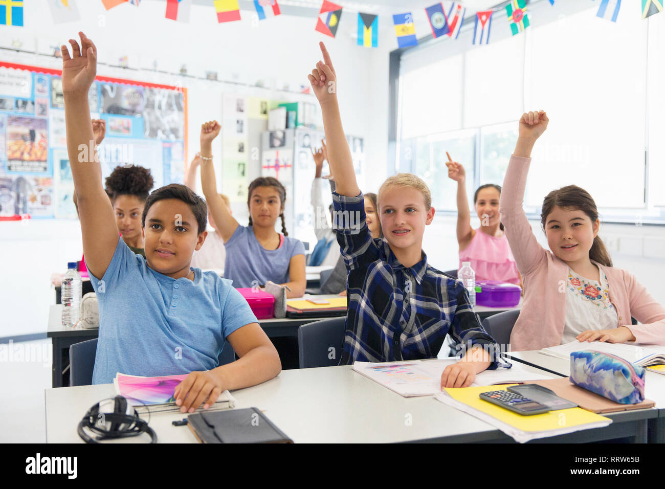 Eager junior high school students with hands raised in classroom Stock Photo