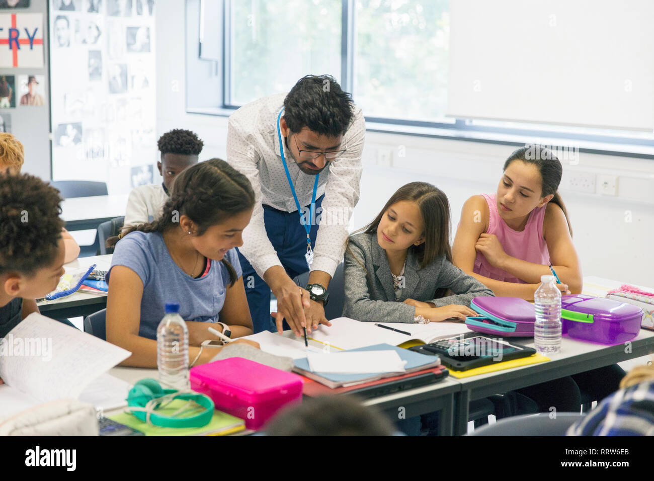 Male teacher helping junior high school girl students at desk in classroom Stock Photo
