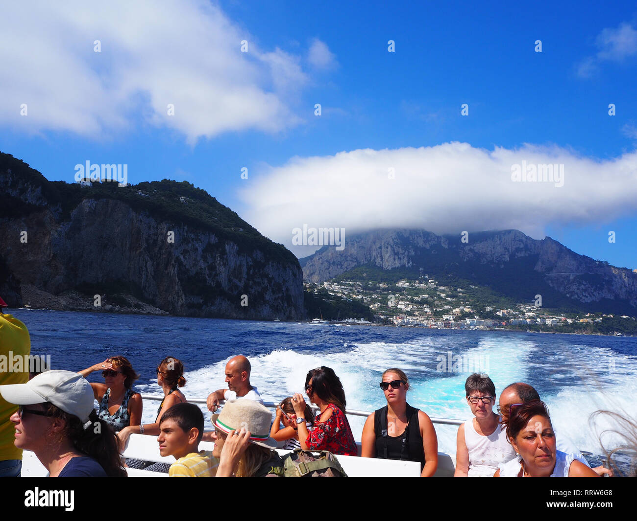 A View of Capri as a boat full of tourists makes its departure after a day trip from Ischia, Italy Stock Photo