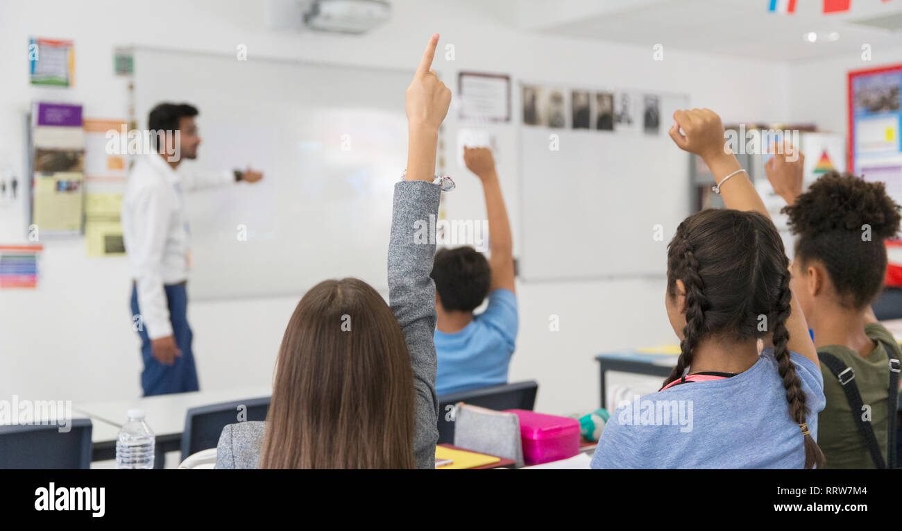 Junior high school students with hands raised during lesson in classroom Stock Photo