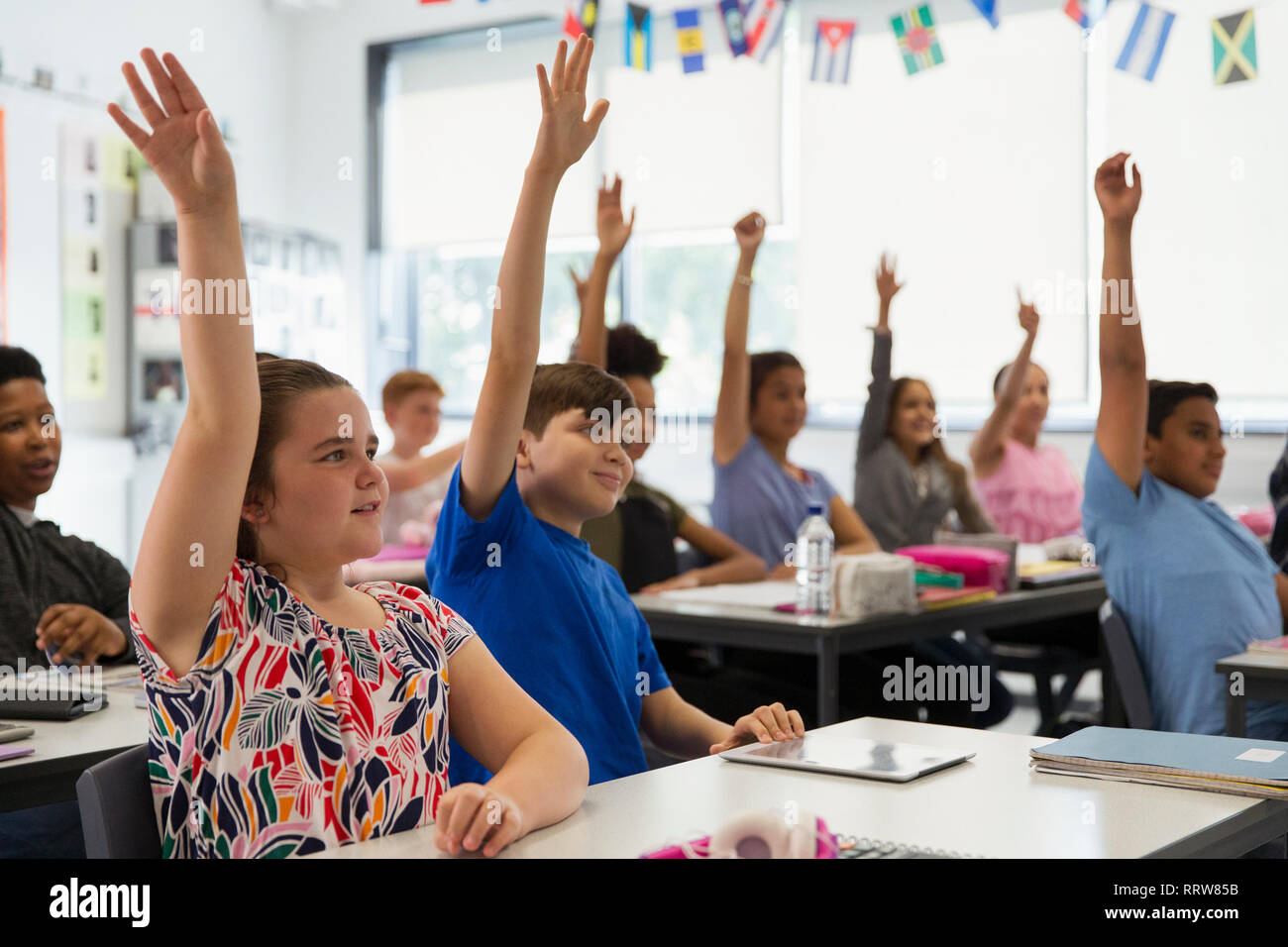 Eager junior high school students with hands raised in classroom Stock Photo