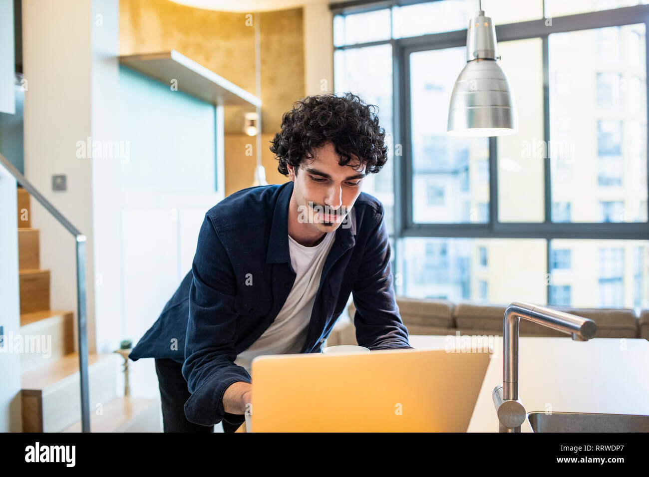 Man using laptop in apartment kitchen Stock Photo