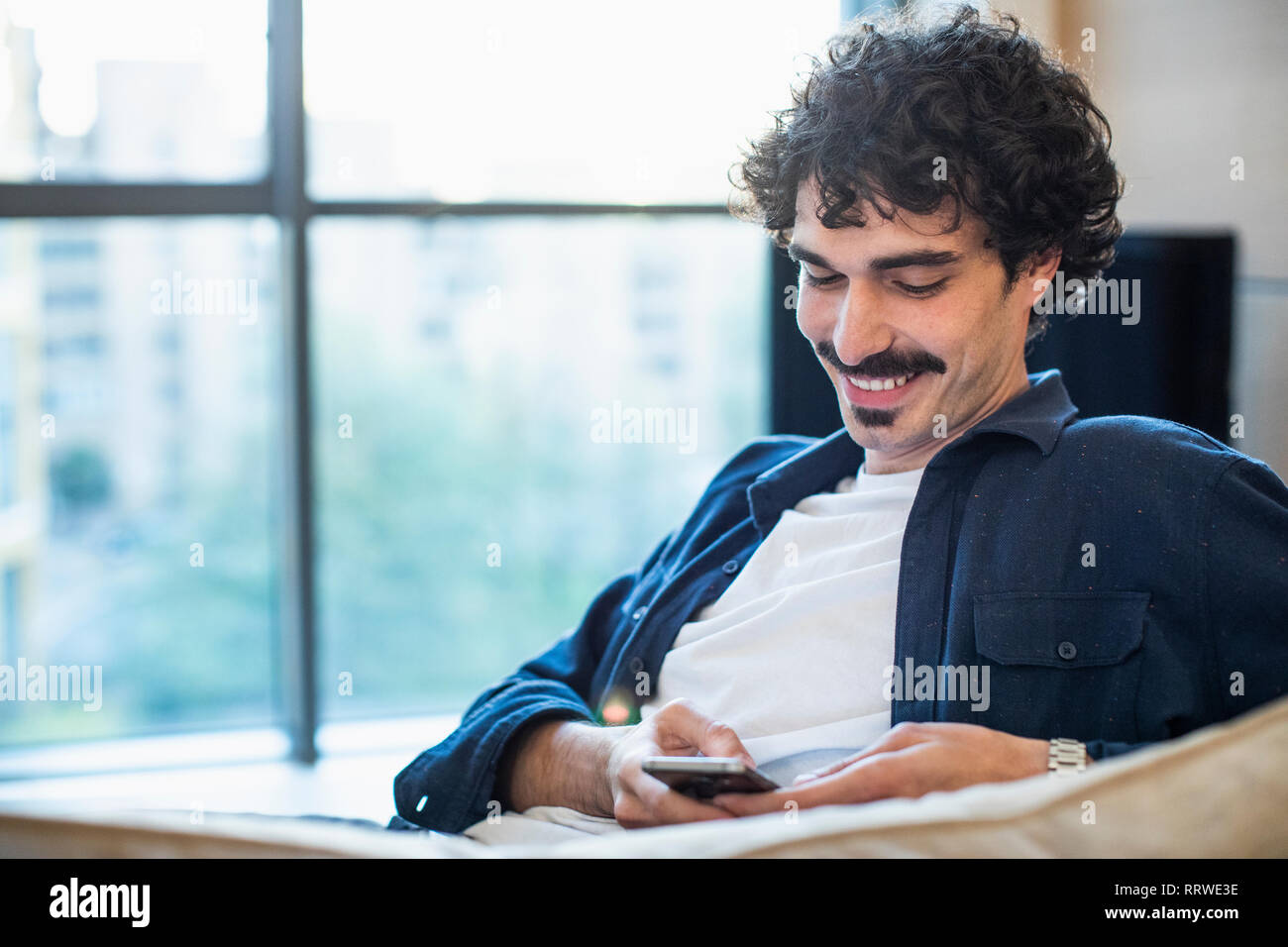 Smiling man using smart phone on sofa Stock Photo