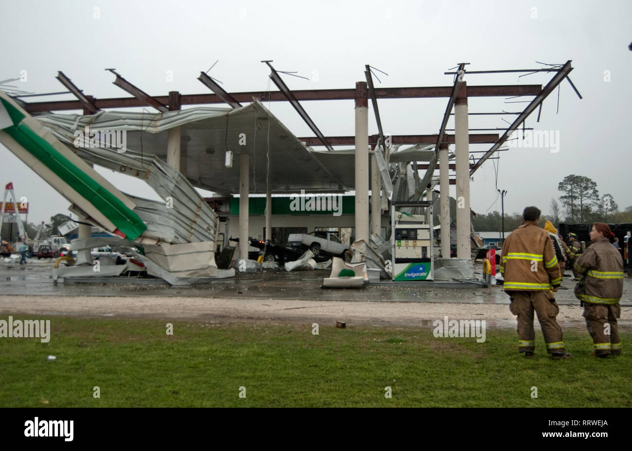 Volunteer firefighters stand in front of a destroyed BP gas station
