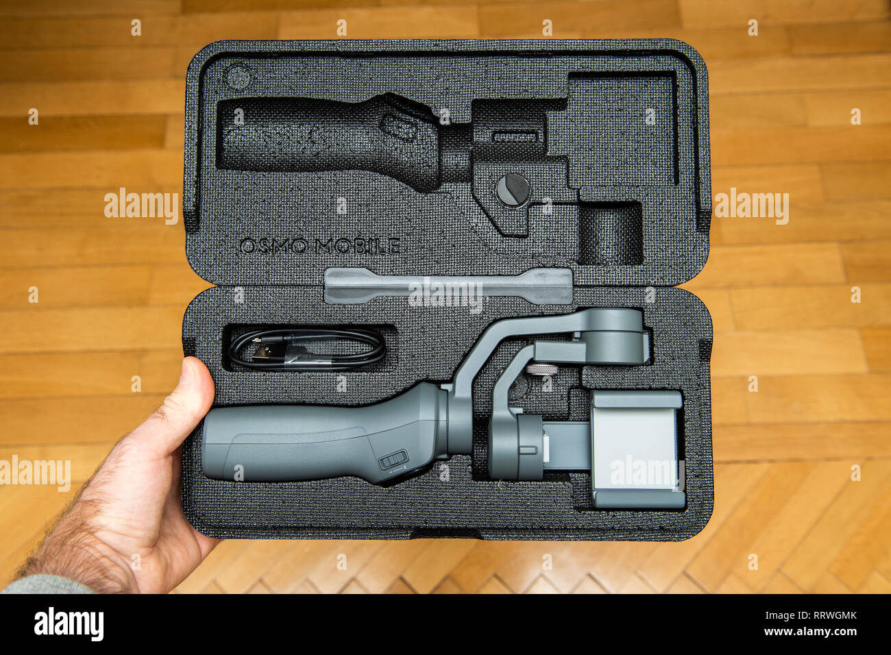 PARIS, FRANCE - NOV 22, 2018: Man unboxing new DJI Osmo Mobile 2 Smartphone Gimbal manufactured by the SZ DJI Technology Co., Ltd company holding the foam packaging above the wooden floor Stock Photo